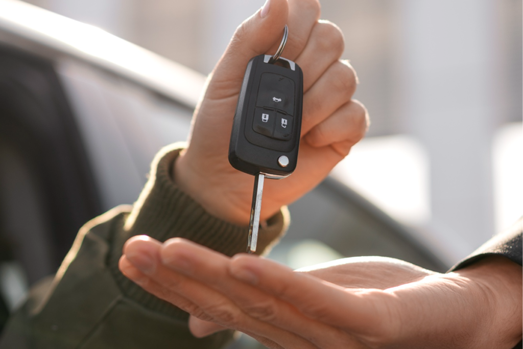 Person handing over a car key fob outside a vehicle, key handover for a car fitted with a Scorpion tracker